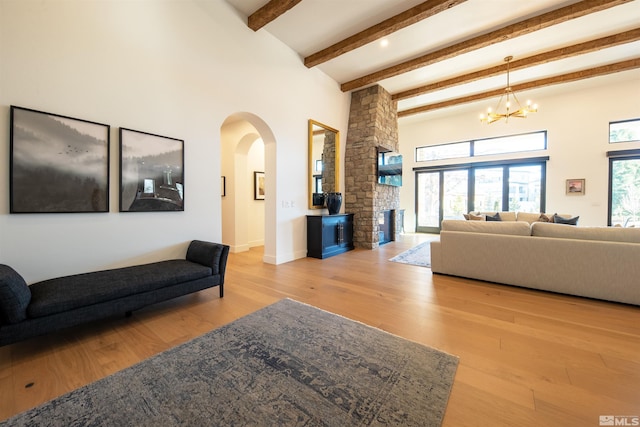 living room with a fireplace, an inviting chandelier, light hardwood / wood-style flooring, a towering ceiling, and beam ceiling