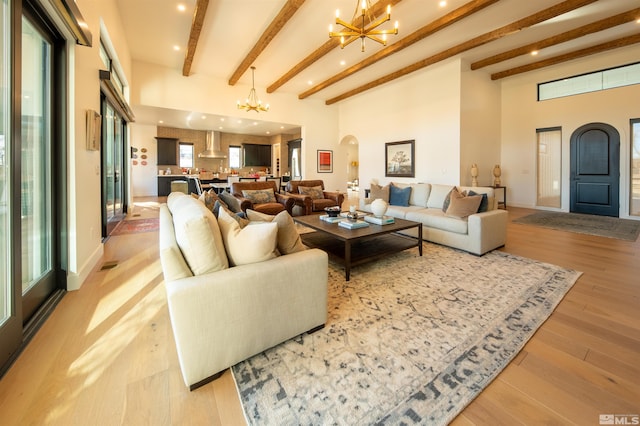 living room featuring beamed ceiling, a chandelier, light hardwood / wood-style floors, and a high ceiling