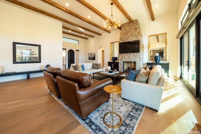 living room featuring a stone fireplace, a chandelier, a towering ceiling, beam ceiling, and light hardwood / wood-style floors