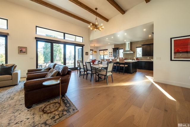 living room featuring beamed ceiling, a high ceiling, an inviting chandelier, and light hardwood / wood-style flooring