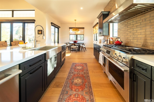 kitchen with sink, light hardwood / wood-style flooring, appliances with stainless steel finishes, hanging light fixtures, and wall chimney exhaust hood