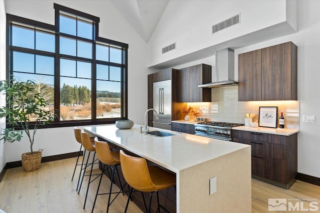 kitchen with a breakfast bar, tasteful backsplash, high quality appliances, a kitchen island with sink, and wall chimney range hood