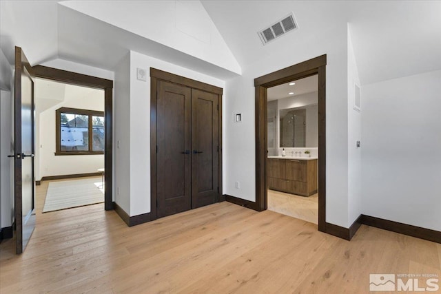 unfurnished bedroom with lofted ceiling, light hardwood / wood-style floors, a closet, and ensuite bathroom