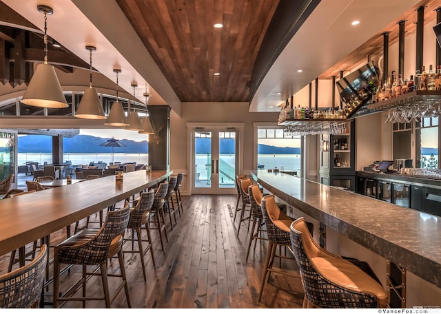 dining area with dark wood-type flooring, french doors, a water view, wooden ceiling, and indoor bar