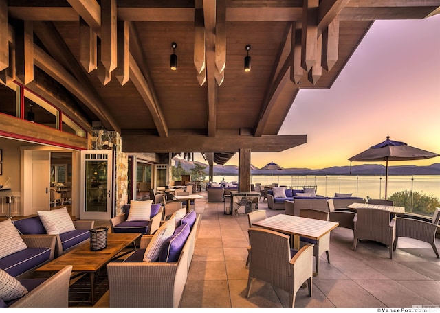 patio terrace at dusk with wine cooler, an outdoor hangout area, and a water view