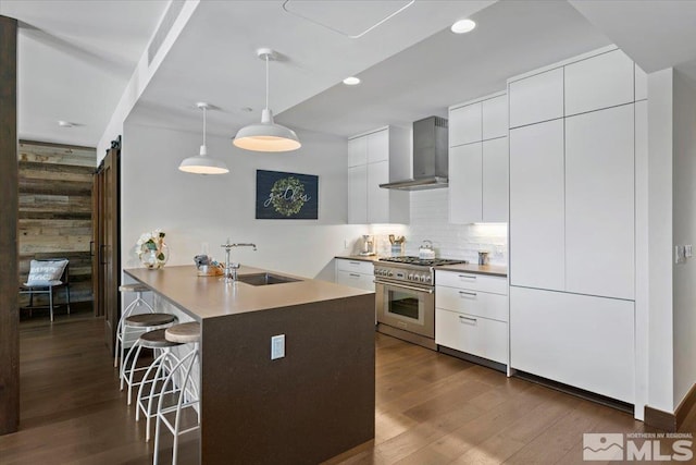 kitchen with white cabinetry, sink, high end range, hanging light fixtures, and wall chimney exhaust hood