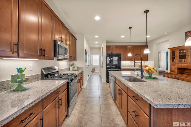 kitchen featuring sink, appliances with stainless steel finishes, hanging light fixtures, light stone countertops, and a center island with sink