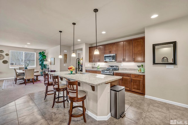 kitchen featuring appliances with stainless steel finishes, a kitchen island with sink, hanging light fixtures, a kitchen breakfast bar, and light tile patterned flooring