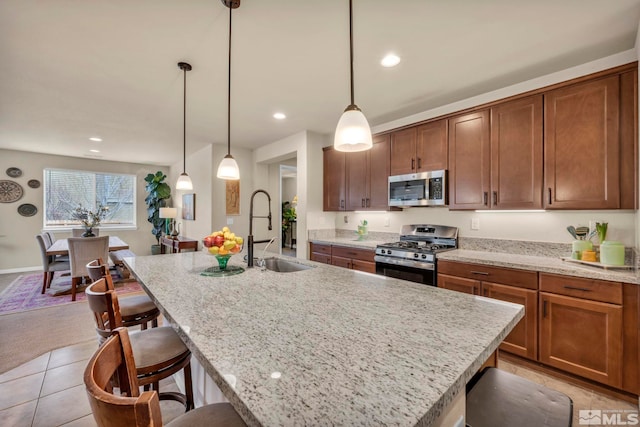 kitchen featuring appliances with stainless steel finishes, an island with sink, sink, hanging light fixtures, and light stone countertops