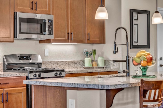 kitchen with light stone counters, appliances with stainless steel finishes, decorative light fixtures, and sink