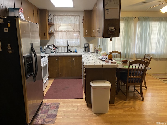 kitchen with sink, light hardwood / wood-style floors, white gas range, stainless steel fridge with ice dispenser, and tile countertops