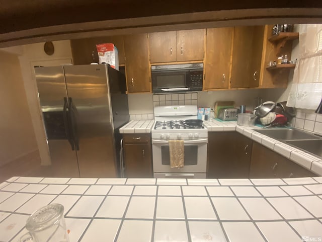 kitchen featuring stainless steel fridge, sink, tile counters, and white gas range oven