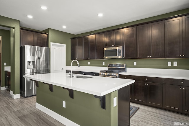 kitchen featuring an island with sink, sink, a kitchen bar, dark brown cabinetry, and stainless steel appliances