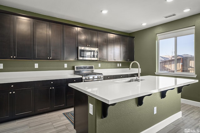 kitchen featuring appliances with stainless steel finishes, a kitchen breakfast bar, sink, and a center island with sink