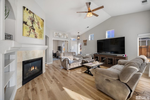 living room featuring ceiling fan, a fireplace, high vaulted ceiling, and light wood-type flooring