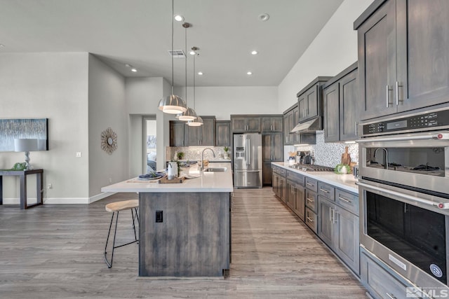 kitchen with appliances with stainless steel finishes, a breakfast bar, hanging light fixtures, hardwood / wood-style flooring, and a center island with sink