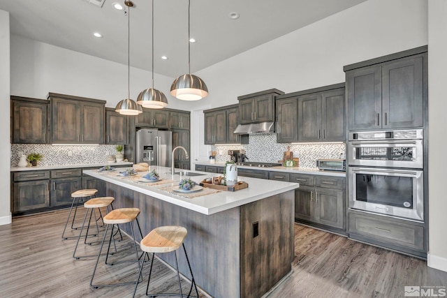 kitchen with a kitchen bar, decorative light fixtures, dark brown cabinets, a center island with sink, and appliances with stainless steel finishes