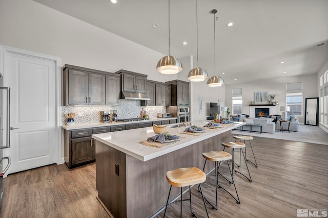 kitchen featuring appliances with stainless steel finishes, a kitchen breakfast bar, hanging light fixtures, light hardwood / wood-style floors, and a center island with sink