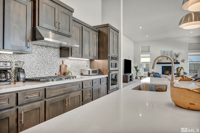 kitchen featuring sink, appliances with stainless steel finishes, hanging light fixtures, tasteful backsplash, and dark brown cabinetry