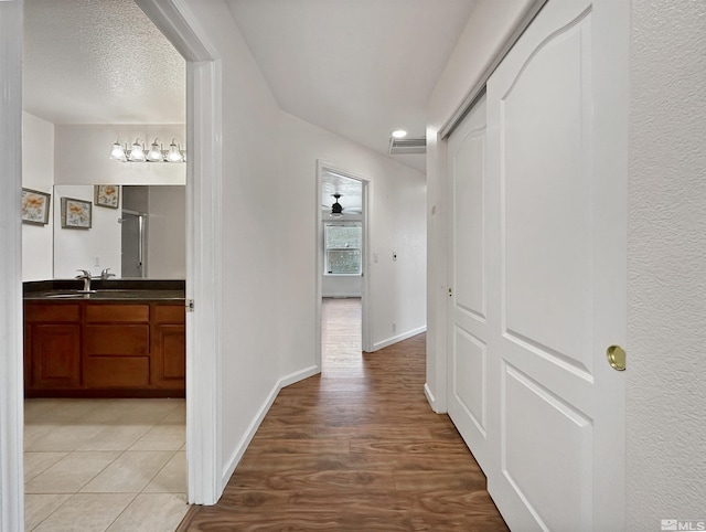 corridor featuring sink, a textured ceiling, and light hardwood / wood-style flooring