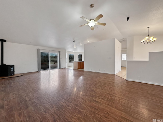 unfurnished living room with lofted ceiling, hardwood / wood-style flooring, ceiling fan with notable chandelier, and a wood stove