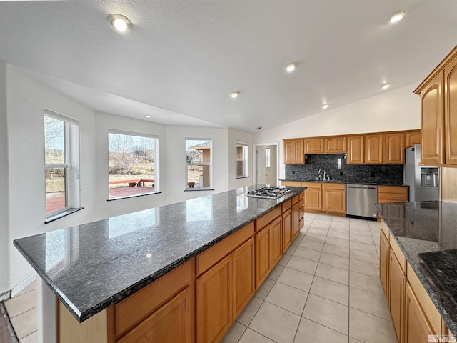 kitchen featuring light tile patterned flooring, a center island, vaulted ceiling, appliances with stainless steel finishes, and dark stone counters