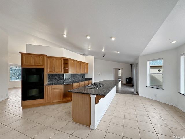 kitchen with vaulted ceiling, double oven, tasteful backsplash, dark stone counters, and a center island