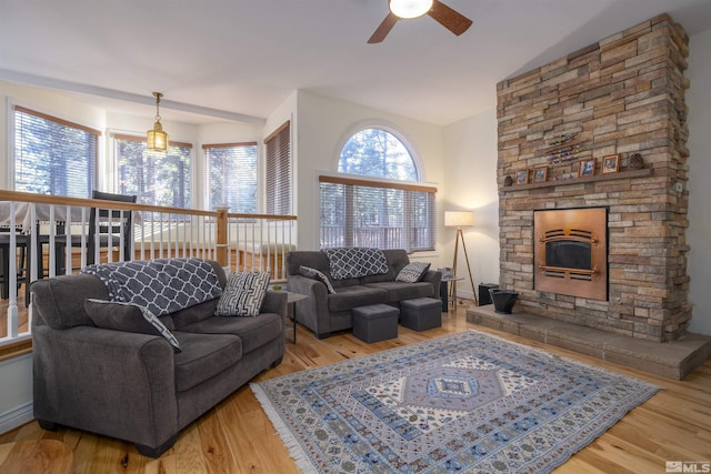 living room with ceiling fan, a stone fireplace, vaulted ceiling, and light hardwood / wood-style flooring