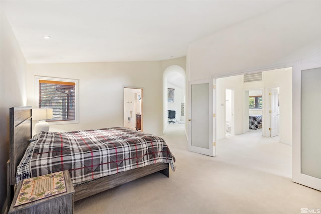 bedroom with lofted ceiling, light colored carpet, and ensuite bathroom