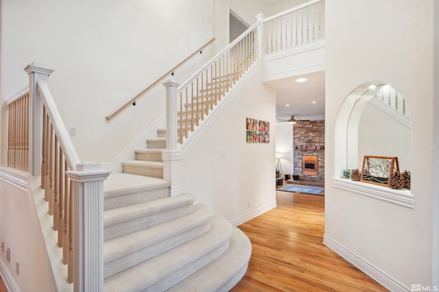 staircase featuring hardwood / wood-style flooring, ceiling fan, a fireplace, and a towering ceiling