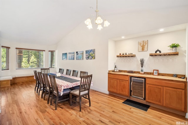 dining area with bar, high vaulted ceiling, a notable chandelier, light hardwood / wood-style floors, and beverage cooler