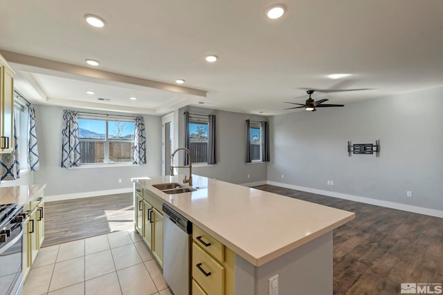 kitchen featuring sink, light hardwood / wood-style flooring, appliances with stainless steel finishes, a tray ceiling, and an island with sink