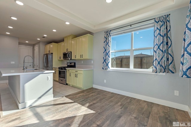 kitchen with appliances with stainless steel finishes, an island with sink, sink, a kitchen bar, and light hardwood / wood-style floors