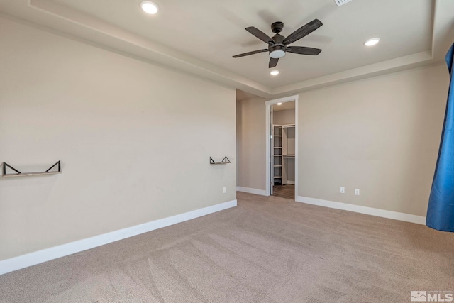 empty room with a raised ceiling, carpet flooring, and ceiling fan