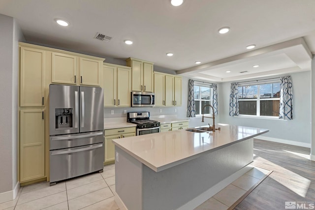 kitchen featuring sink, appliances with stainless steel finishes, cream cabinets, an island with sink, and light tile patterned flooring