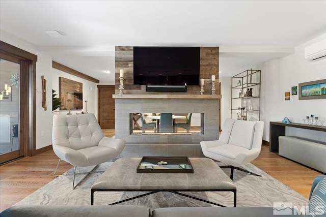 living room with a multi sided fireplace, an AC wall unit, and light wood-type flooring