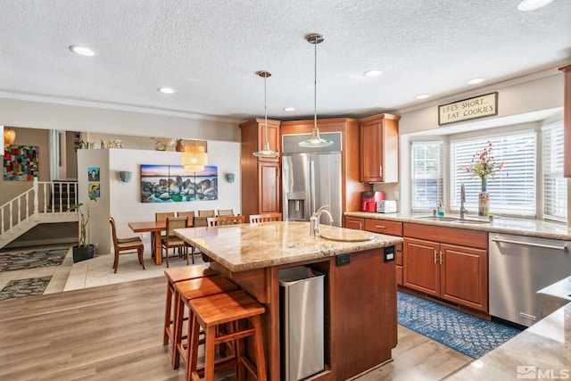 kitchen featuring appliances with stainless steel finishes, decorative light fixtures, an island with sink, sink, and light wood-type flooring