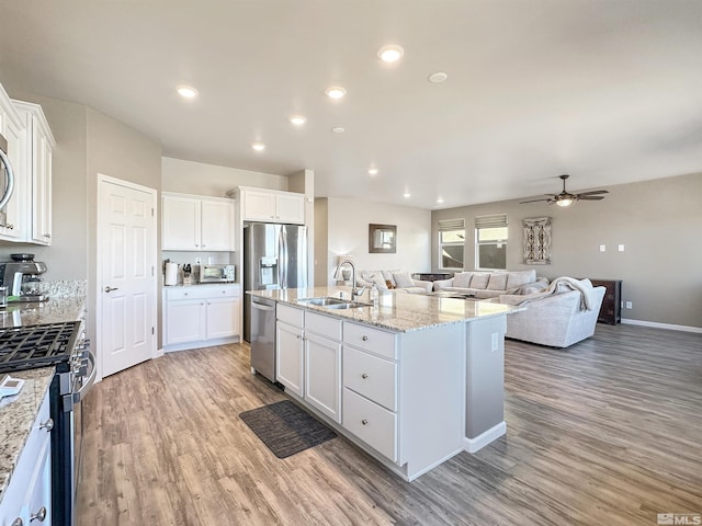 kitchen with sink, white cabinetry, light wood-type flooring, appliances with stainless steel finishes, and a kitchen island with sink