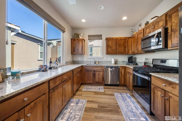 kitchen featuring stainless steel appliances, sink, light stone counters, and light hardwood / wood-style flooring