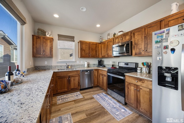 kitchen with light stone countertops, appliances with stainless steel finishes, sink, and light hardwood / wood-style floors