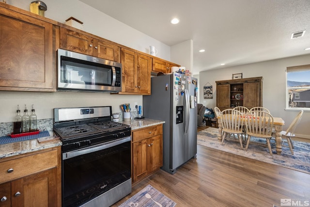 kitchen featuring dark wood-type flooring, appliances with stainless steel finishes, and light stone countertops