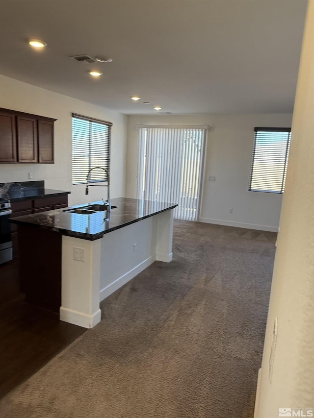 kitchen with sink, stainless steel range with electric stovetop, dark brown cabinets, dark carpet, and an island with sink