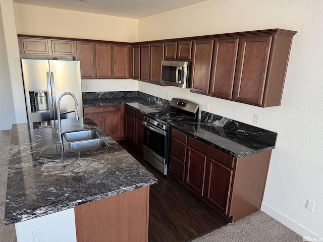 kitchen featuring sink, stainless steel appliances, dark stone counters, and dark colored carpet