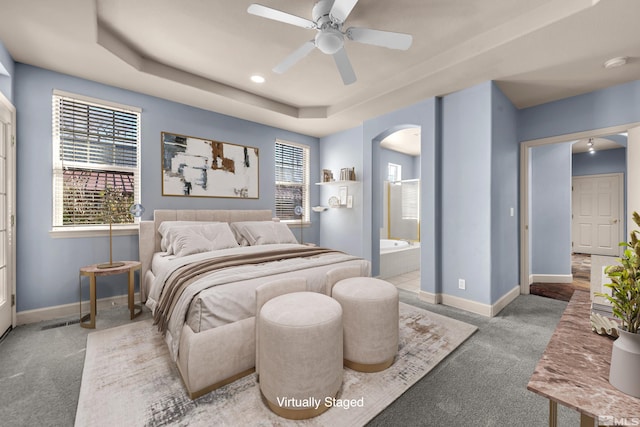 carpeted bedroom featuring ceiling fan, connected bathroom, a raised ceiling, and multiple windows