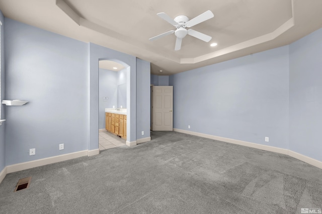 unfurnished bedroom with ceiling fan, ensuite bathroom, and a tray ceiling