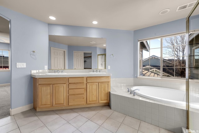 bathroom with tile patterned flooring, vanity, and a relaxing tiled tub