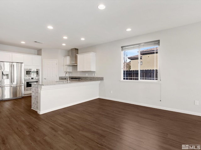 kitchen featuring dark wood-type flooring, appliances with stainless steel finishes, white cabinetry, kitchen peninsula, and wall chimney exhaust hood