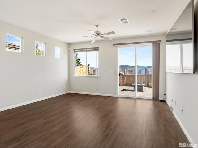 spare room featuring a mountain view, dark wood-type flooring, ceiling fan, and plenty of natural light