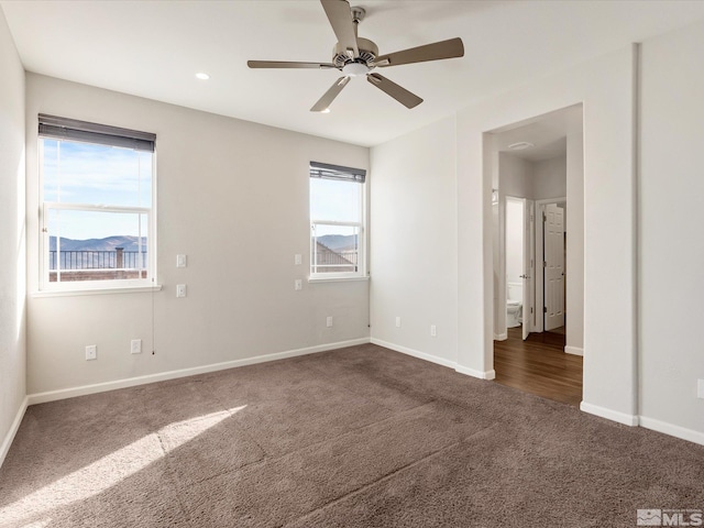 unfurnished bedroom with multiple windows, dark colored carpet, and ceiling fan