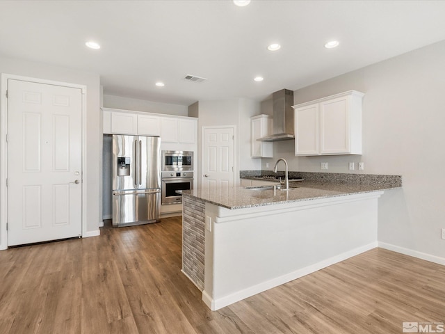 kitchen with wall chimney exhaust hood, white cabinetry, stainless steel appliances, and kitchen peninsula